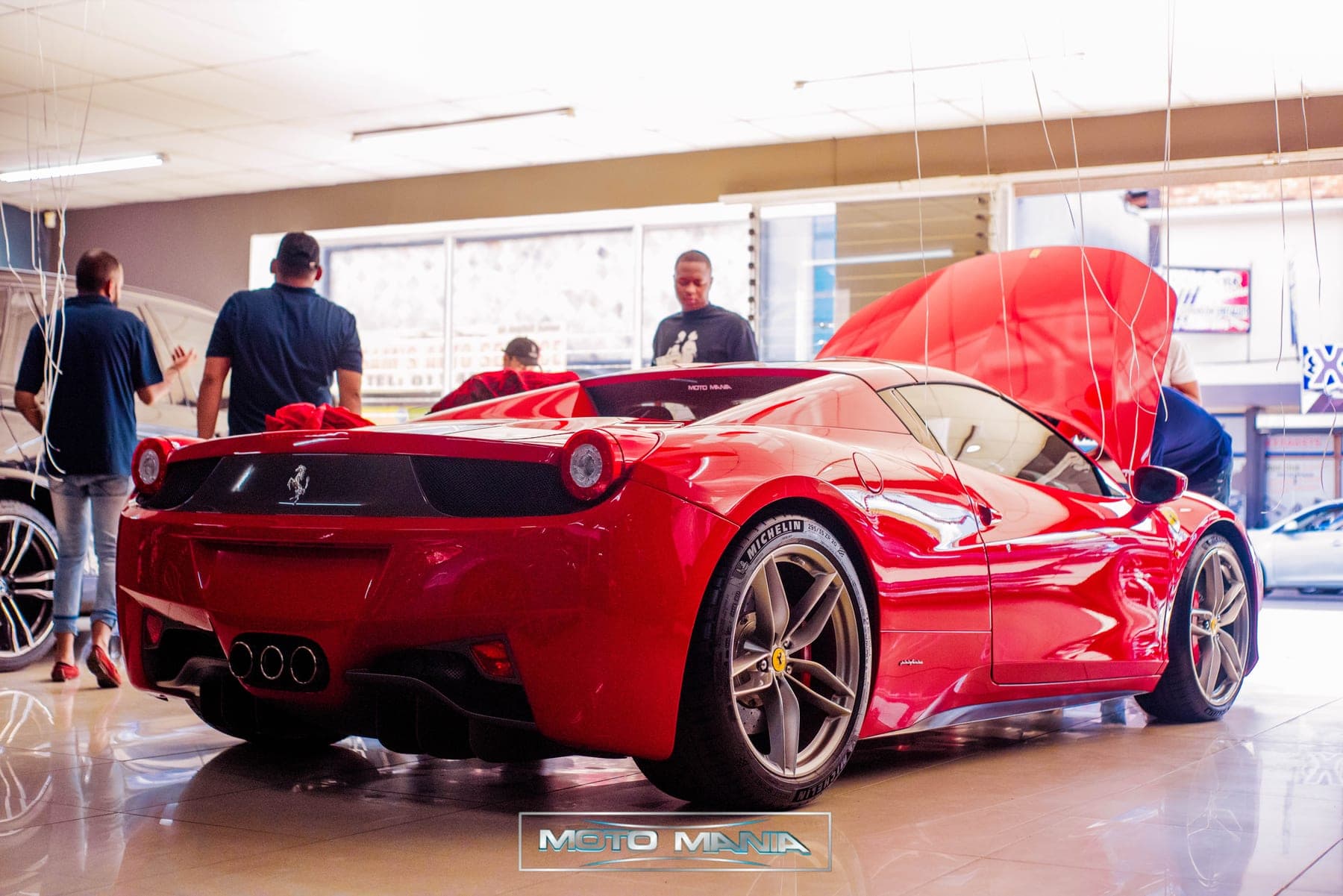 Red Ferrari 458 from behind with its engine cover open in a showroom