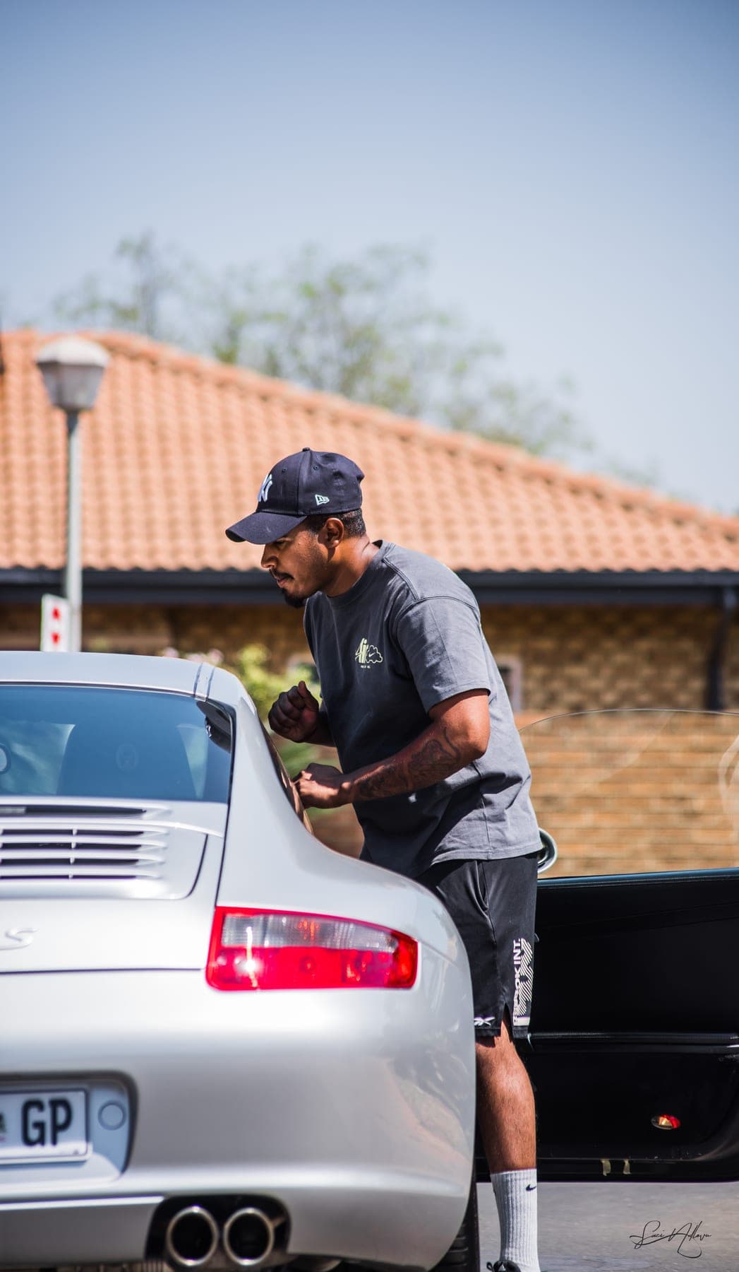 Detailer in a cap at the tail of a Porsche 911