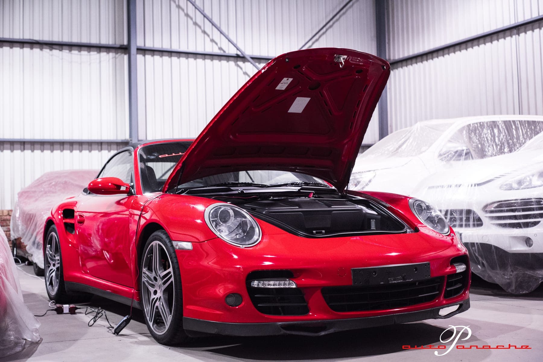 Red Porsche 911 Turbo with its bonnet open among covered cars