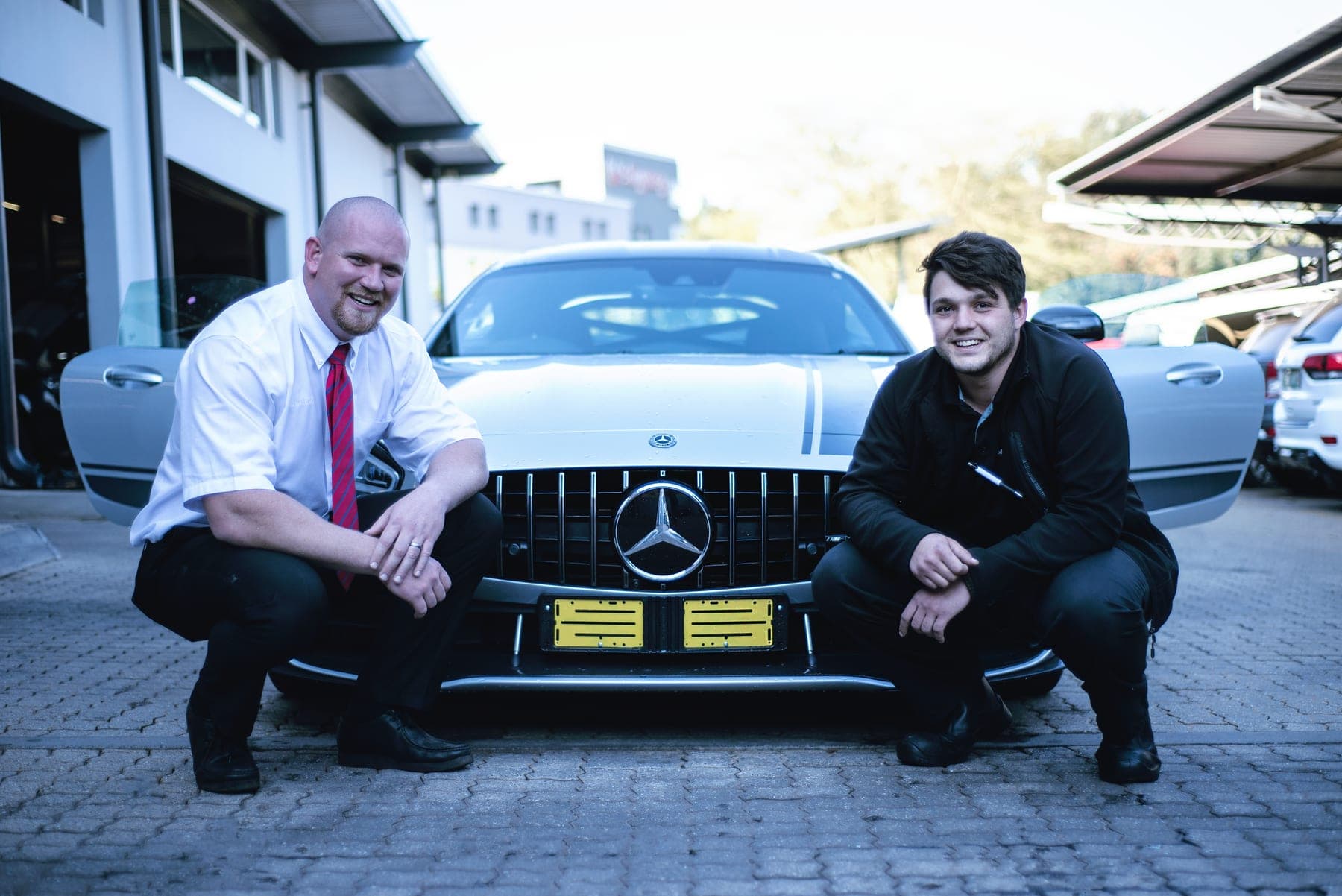 Two men crouched beside a Mercedes-AMG GT at handover