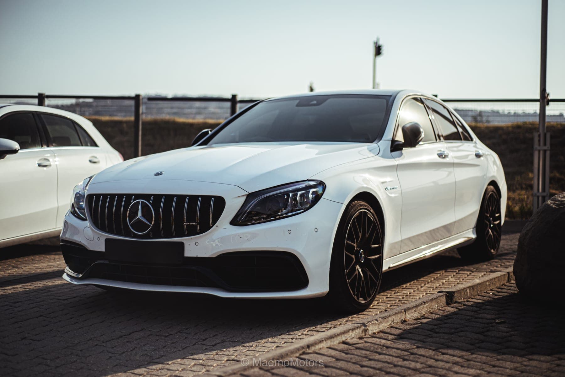White Mercedes-AMG C63 on black wheels at the water's edge