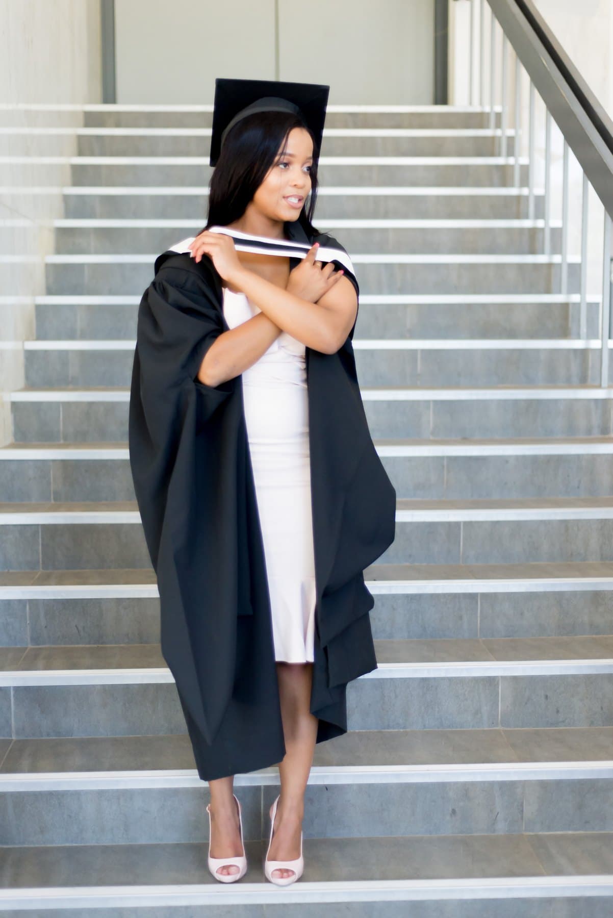Graduate on the stairs, gown over a blush dress
