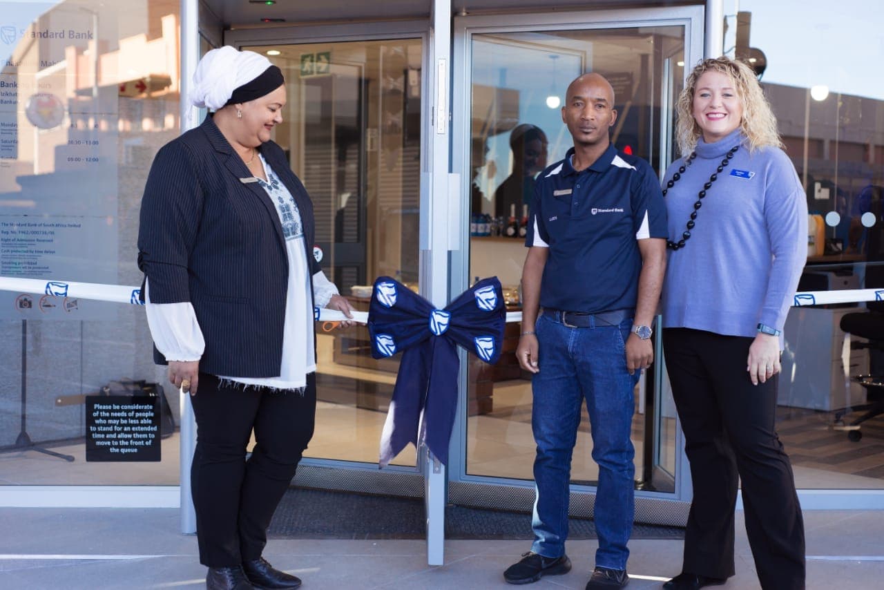 Three guests beside the blue ribbon at a Standard Bank branch opening