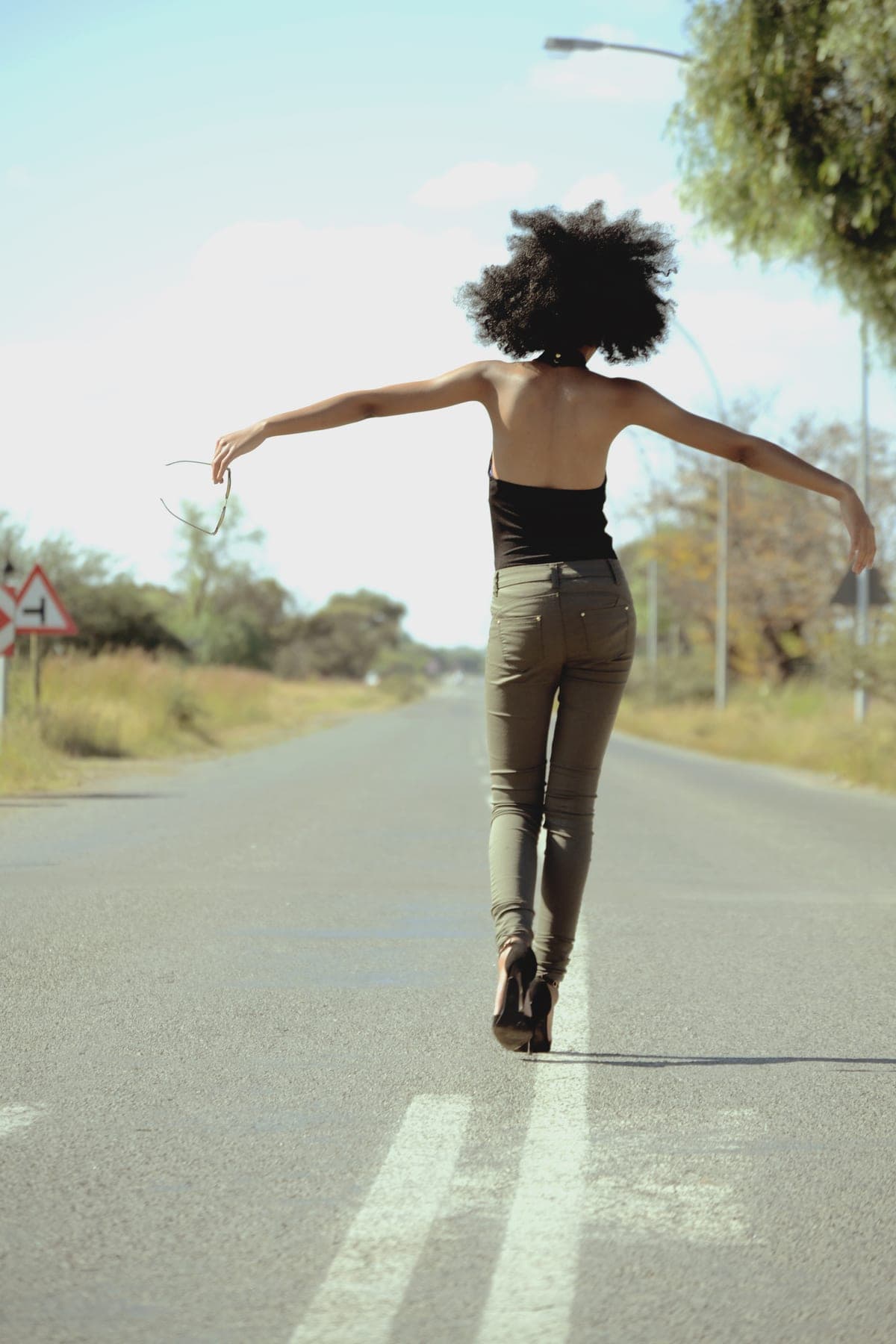 Afro and arms out, walking the centre line of an empty road in heels