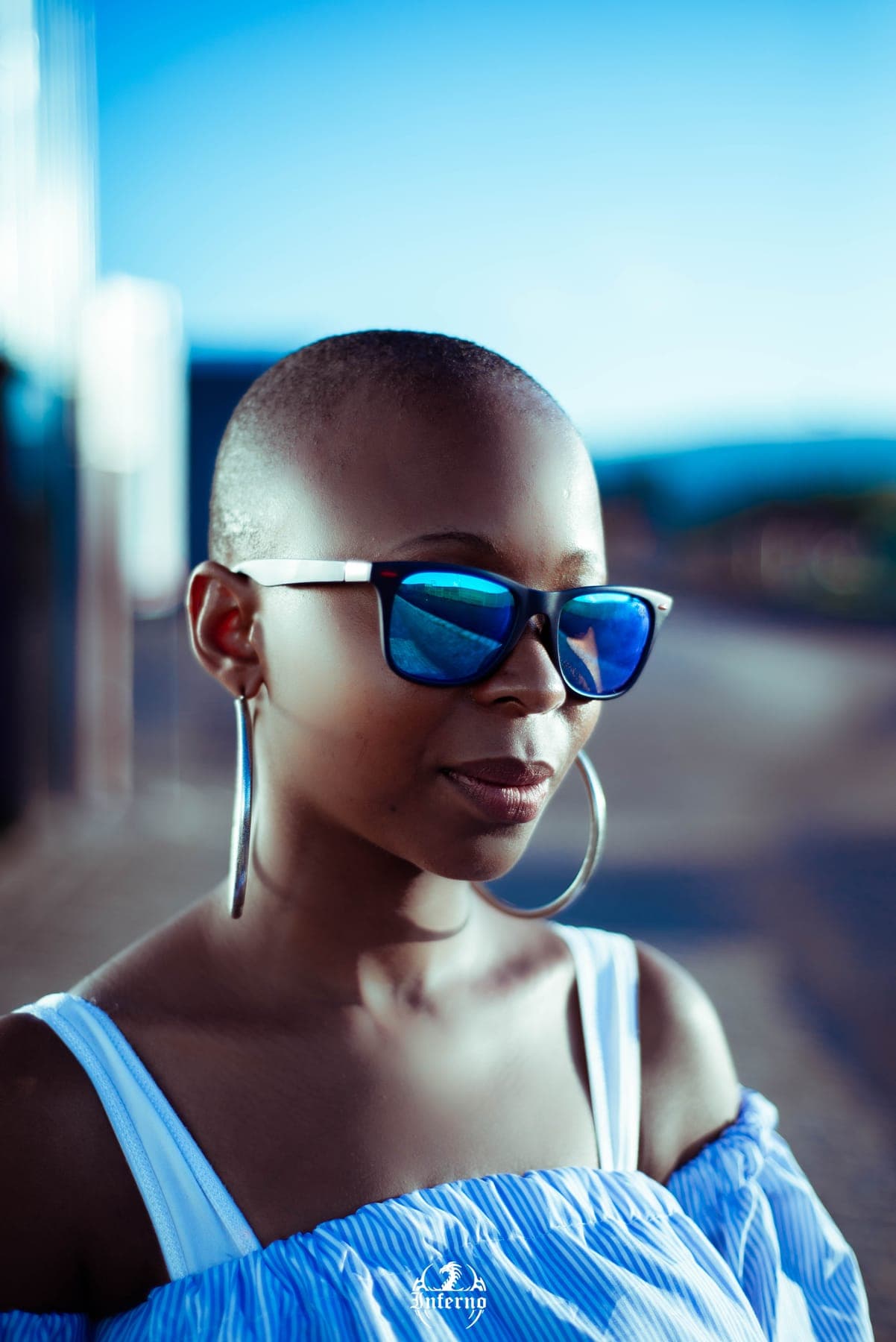 Woman in blue mirrored sunglasses and hoops against a blue sky