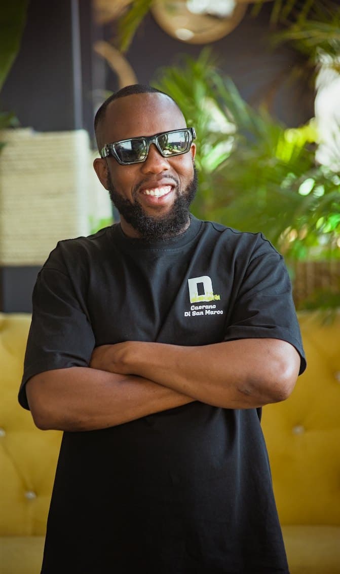 Man in dark glasses smiling with arms crossed on a yellow couch