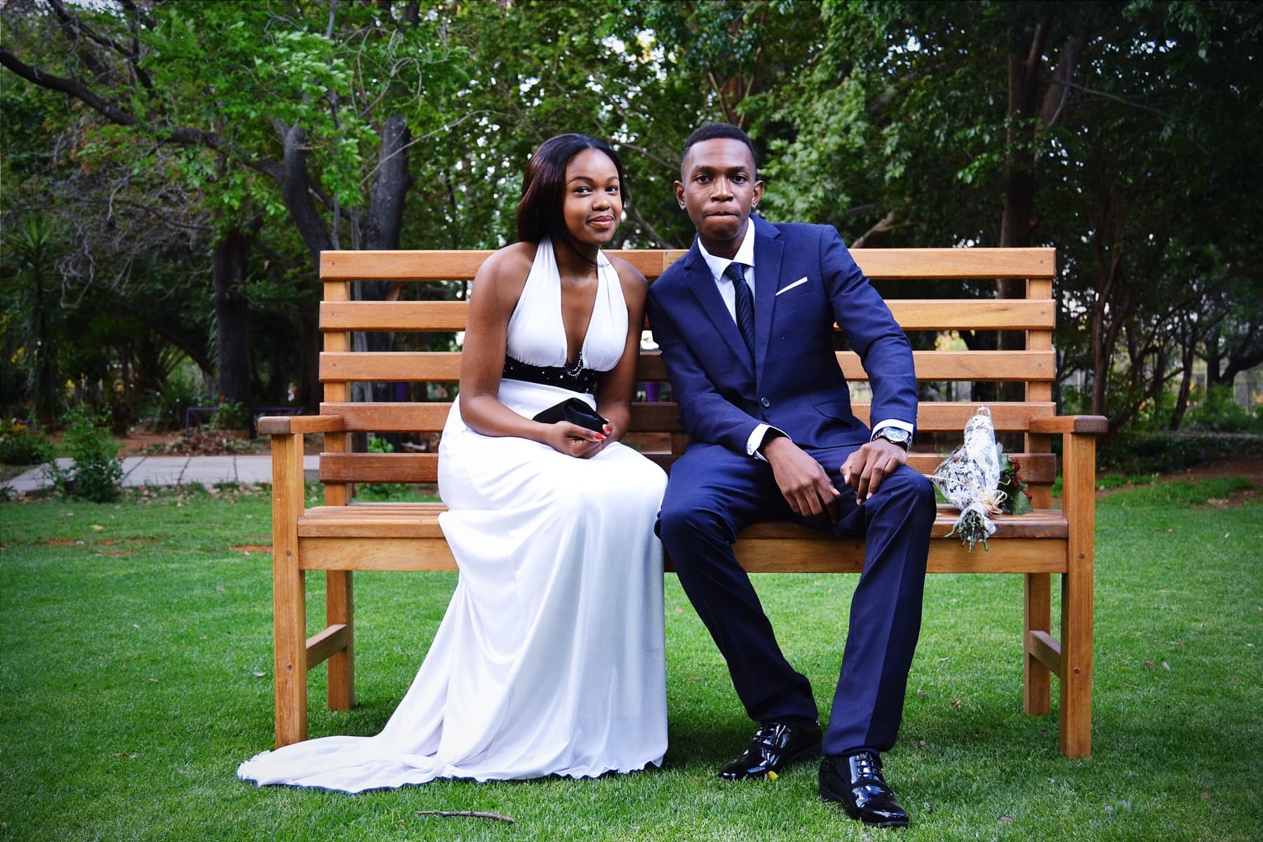 Matric dance couple seated on the bench, flowers beside him