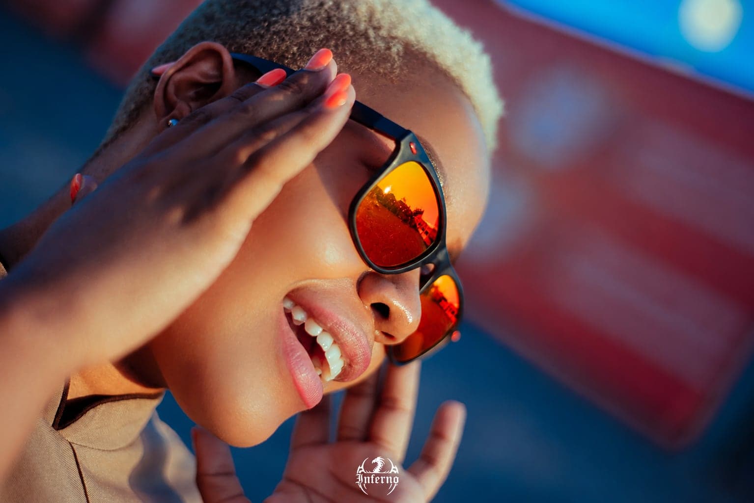 Laughing in red mirrored Inferno lenses, hand raised to the sun