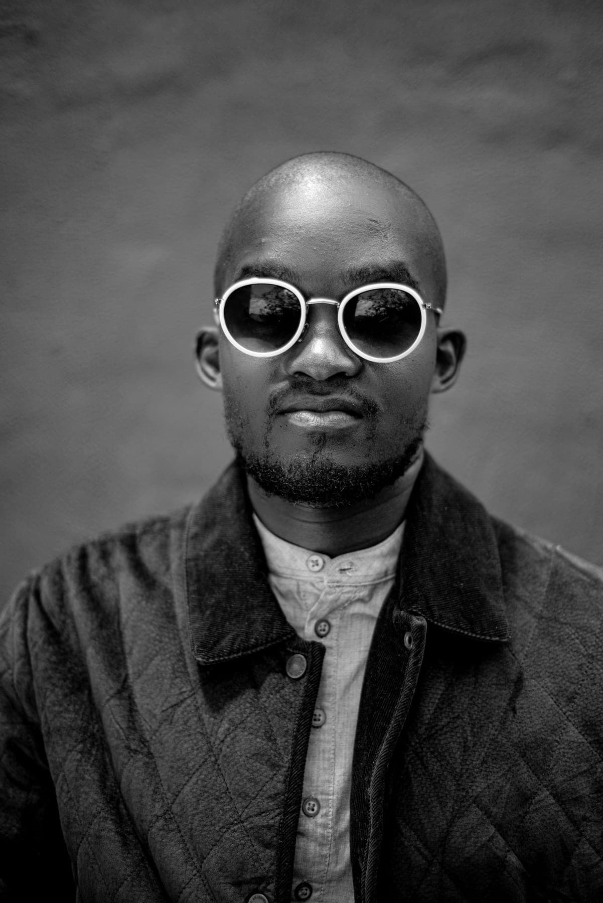 Black and white portrait in round white-rimmed sunglasses and a quilted jacket