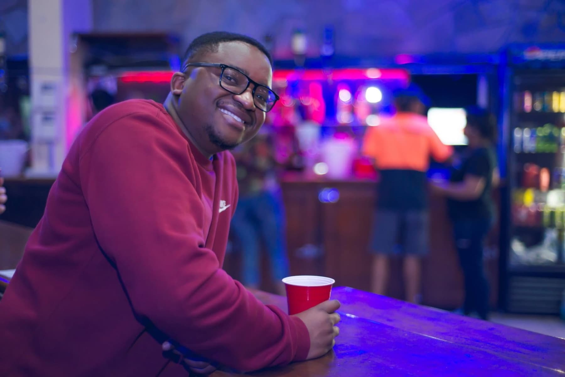 Sipping from a red cup at the bar under blue and pink light