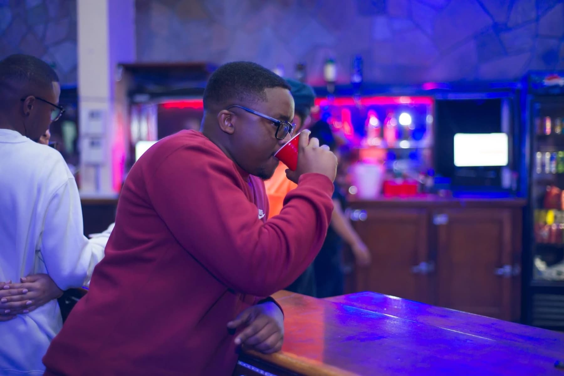 Grinning at the bar with a red cup, lights behind