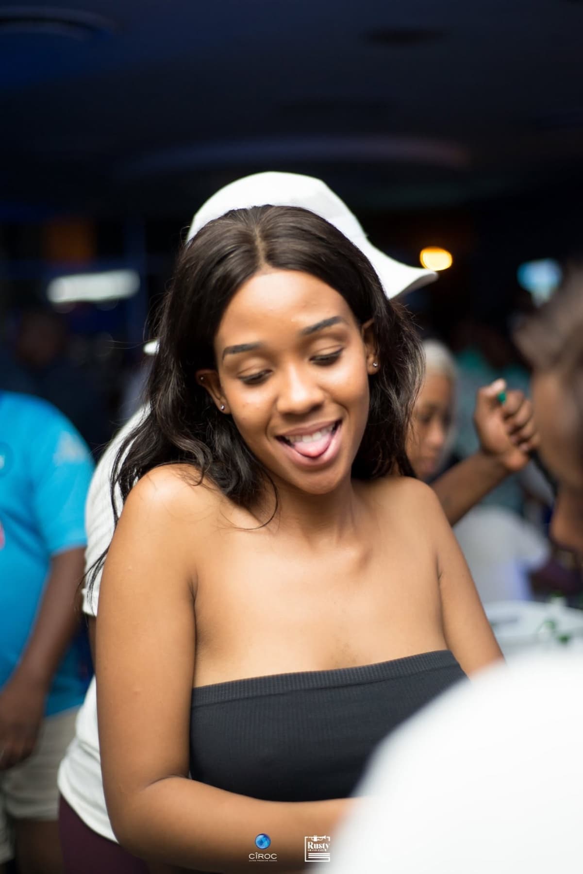 White cap, tongue out, mid-laugh in a blue room