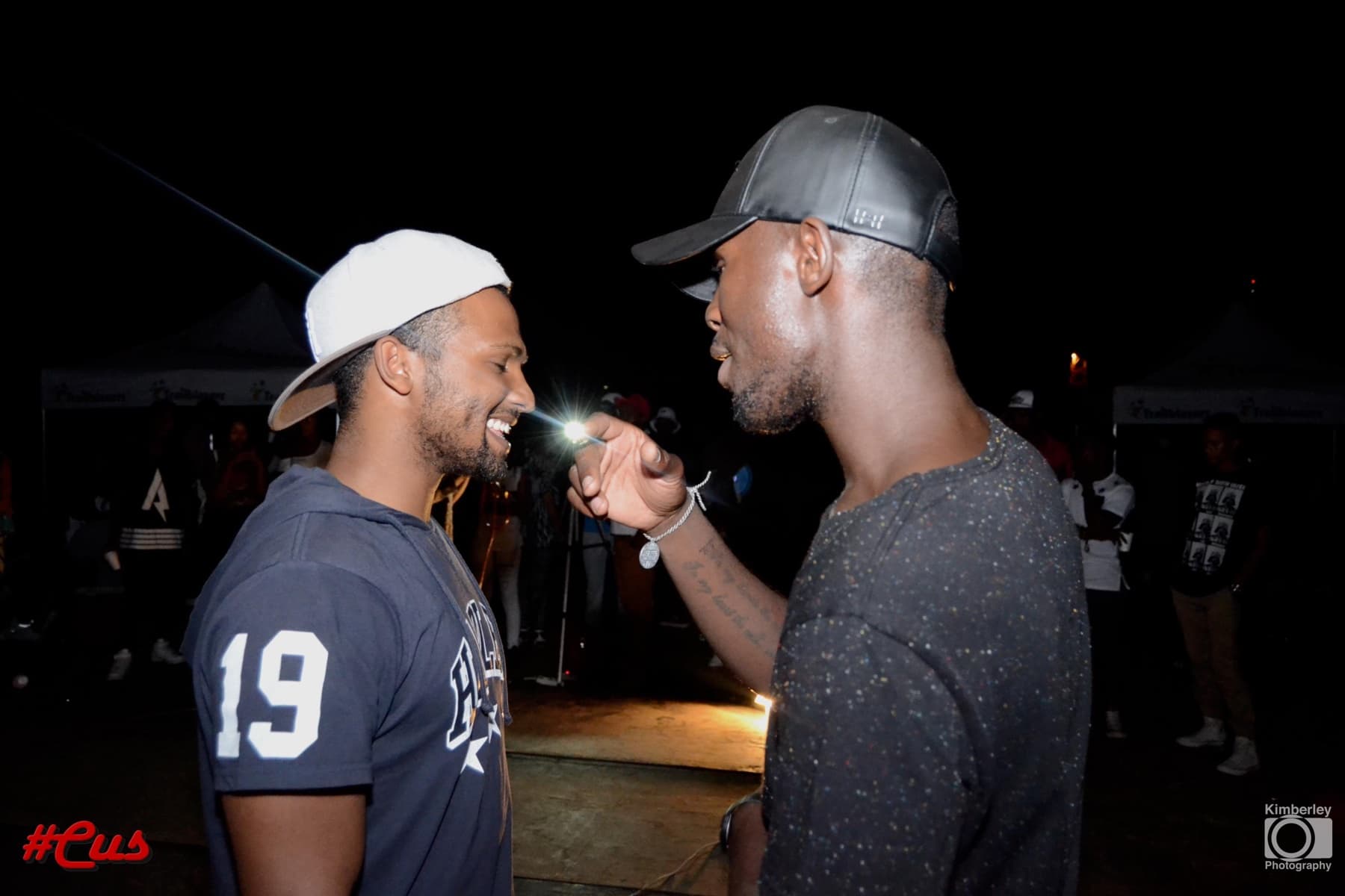 Two friends laughing face to face under a white cap and a leather one at #Cus