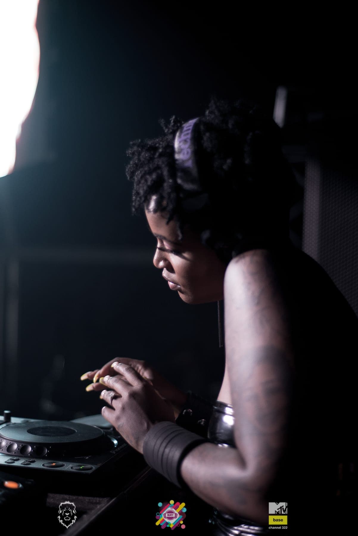 DJ in profile at the decks, light on her braids