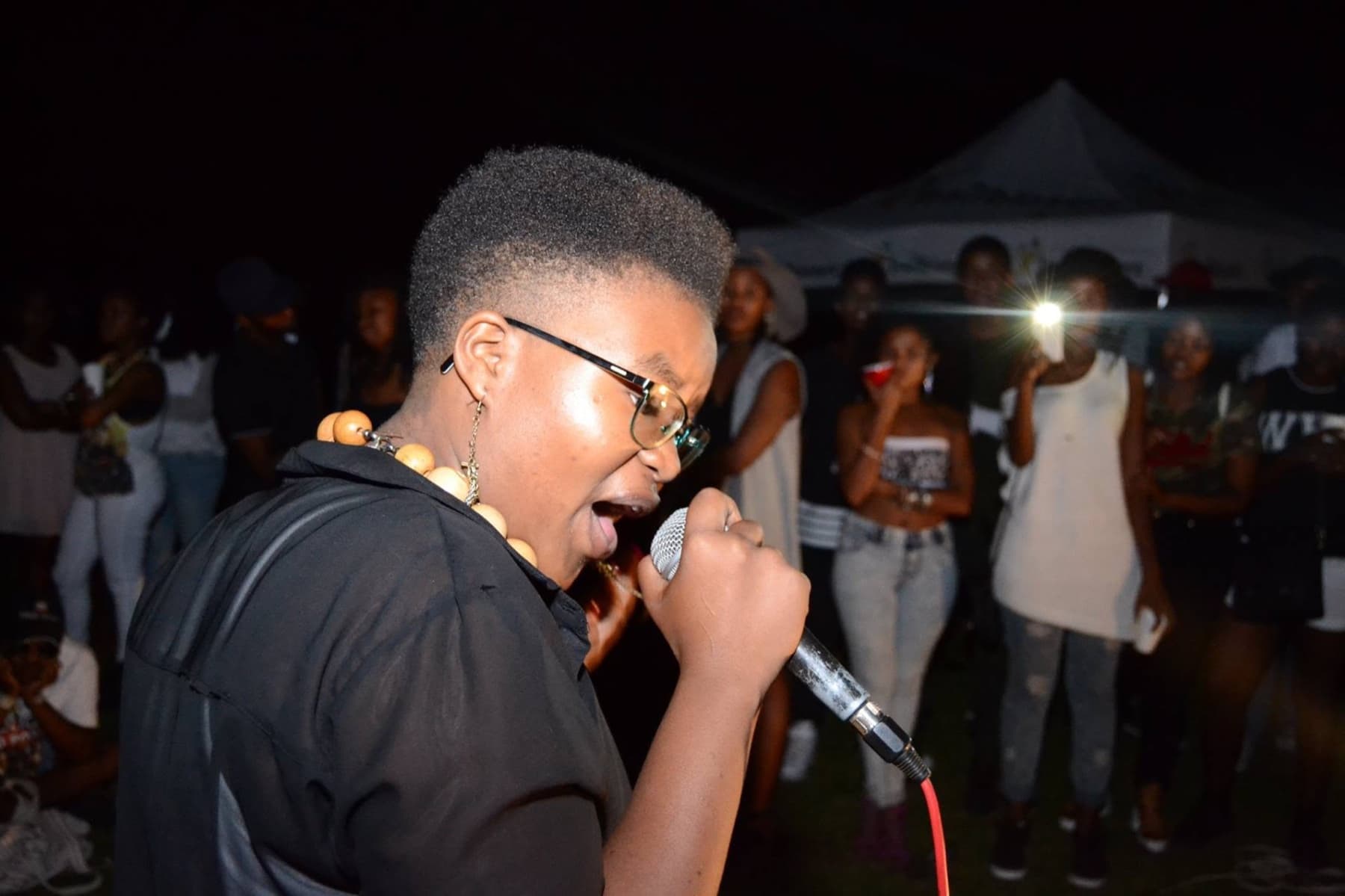 Singer in glasses and wooden beads on the mic, phones up behind
