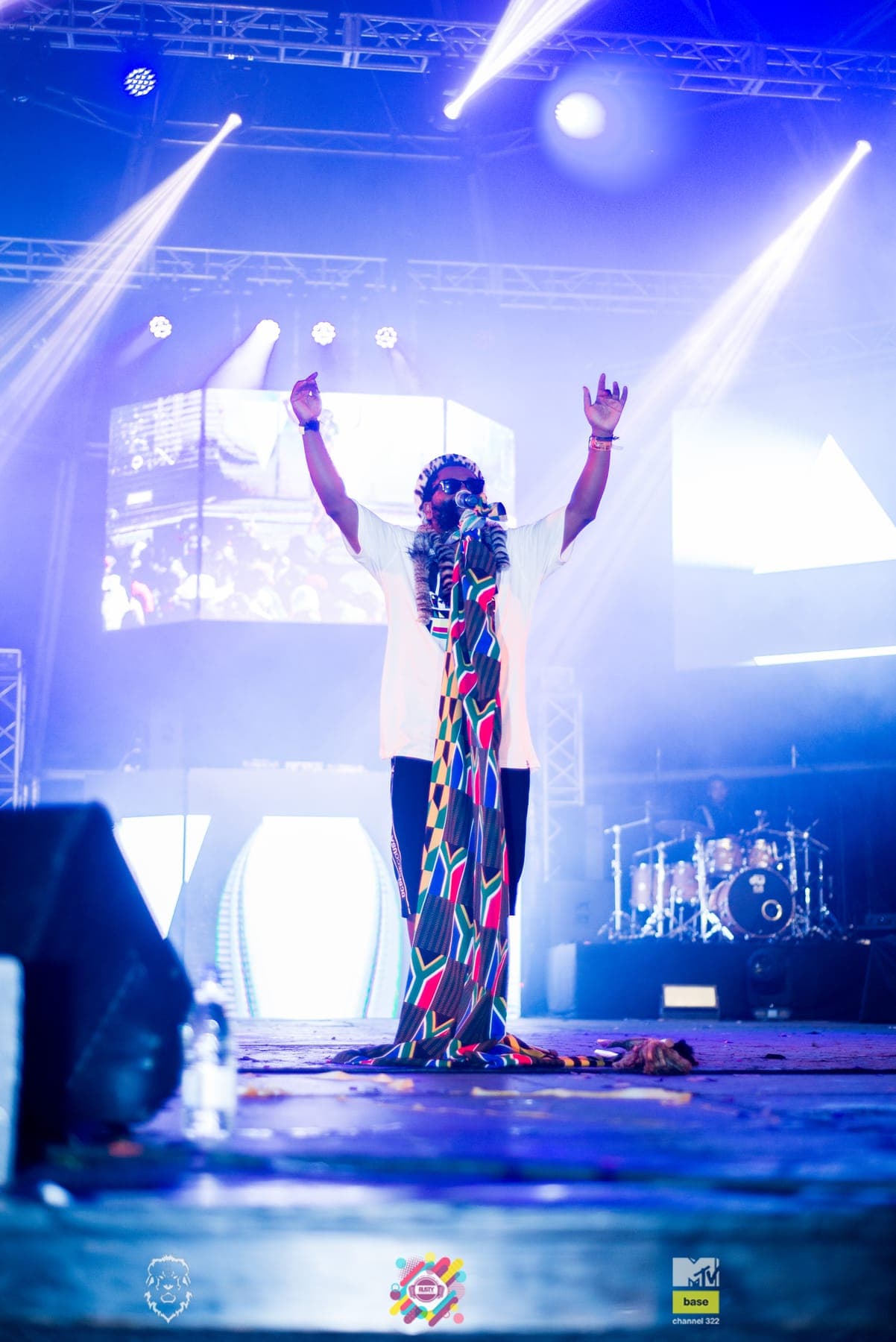 Sjava with both arms raised under blue stage light