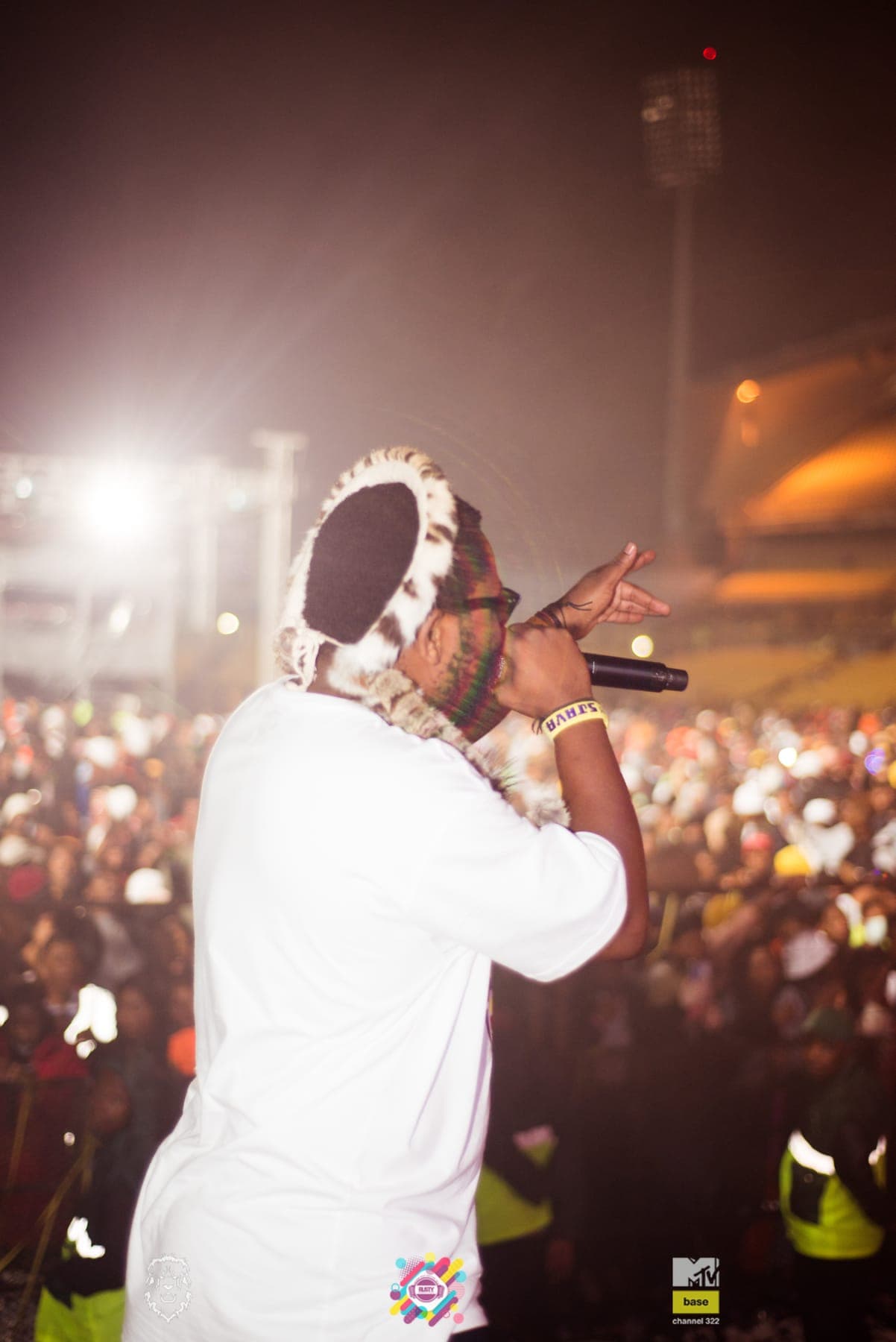 Sjava in white at the stage edge, the stadium crowd behind him