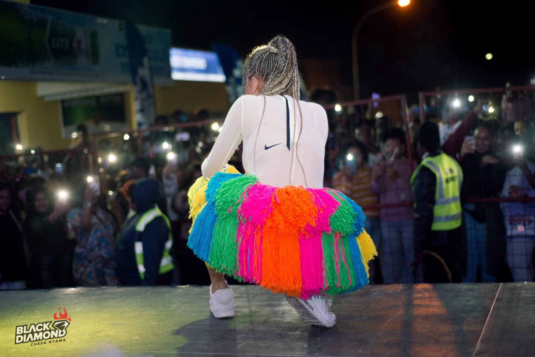 Performer in a neon tassel skirt above a stadium crowd