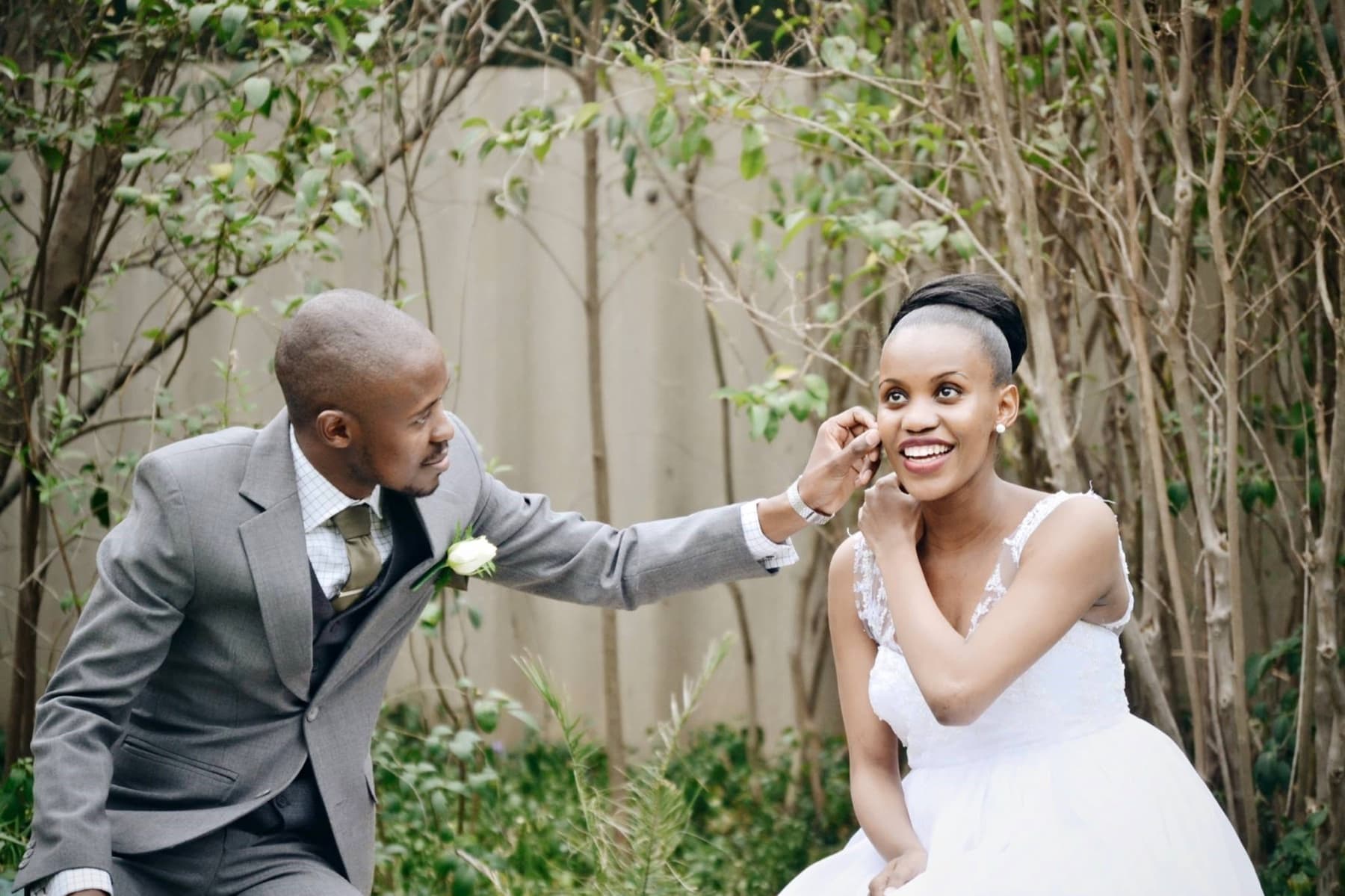 Groom reaching to fix the bride's earring in a garden