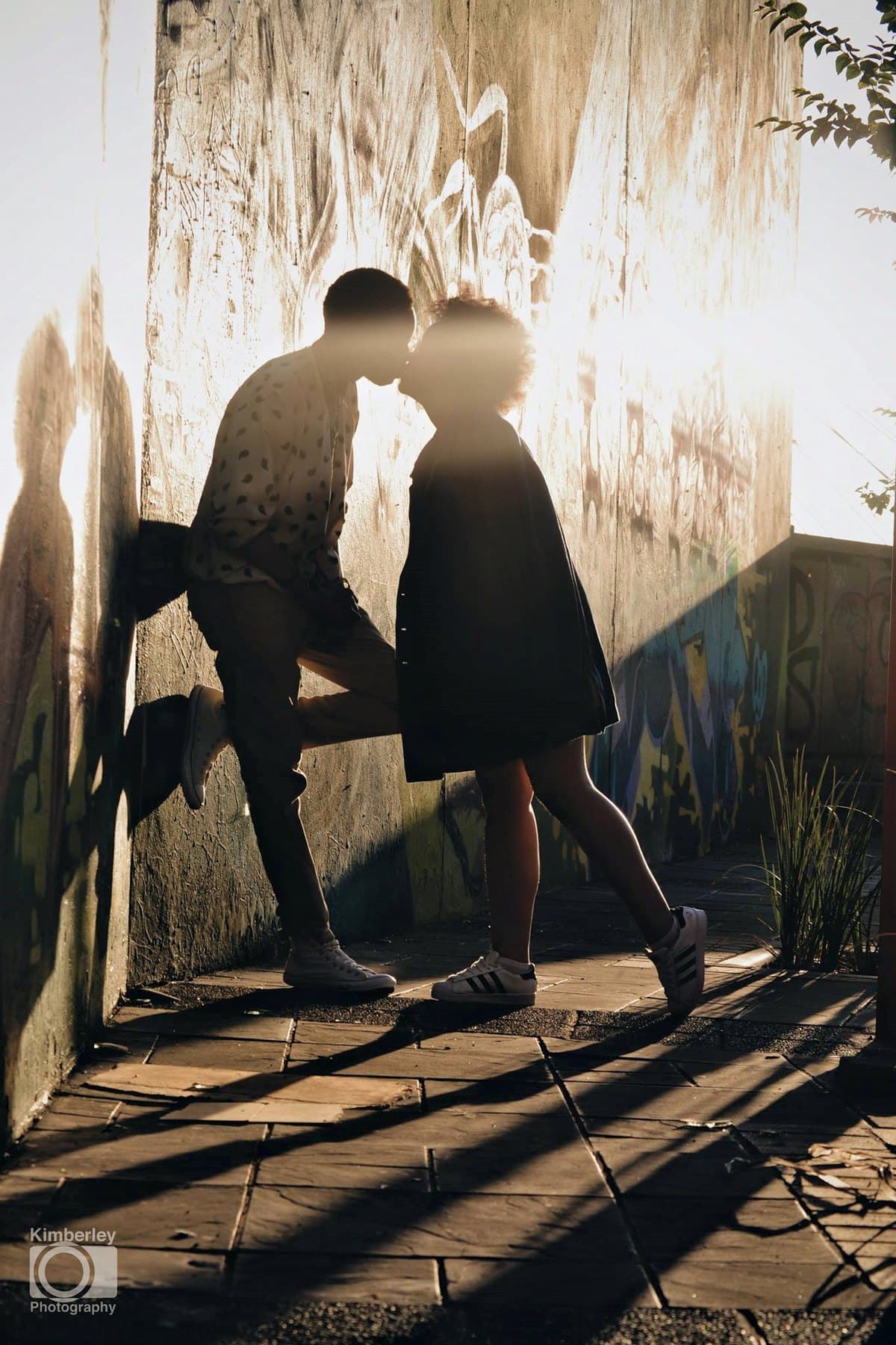 A kiss against a sunlit graffiti wall