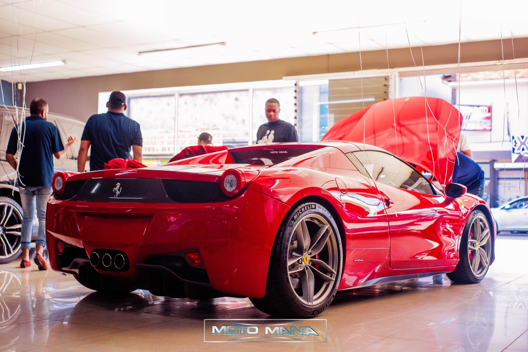 Red Ferrari 458 from behind with its engine cover open in a showroom