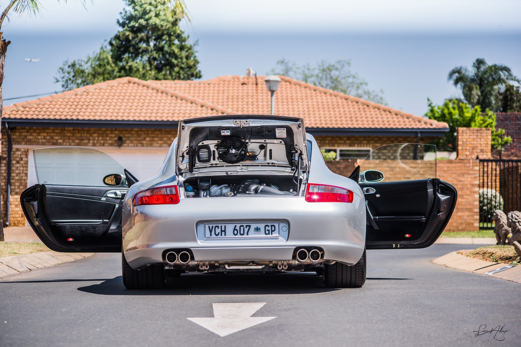 Silver Porsche 911 with both doors open in a driveway