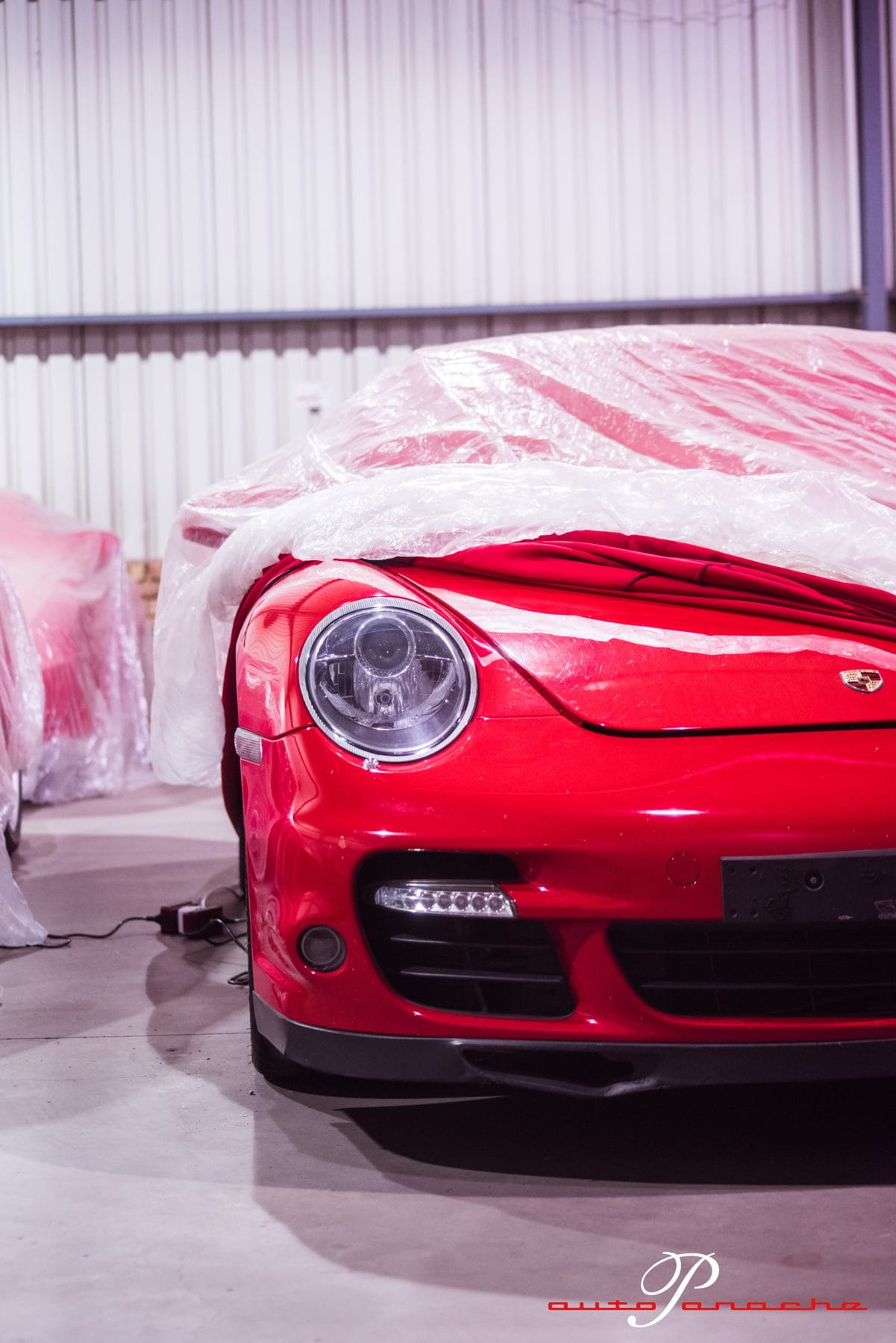 Red Porsche 911 Turbo nose beside covered cars