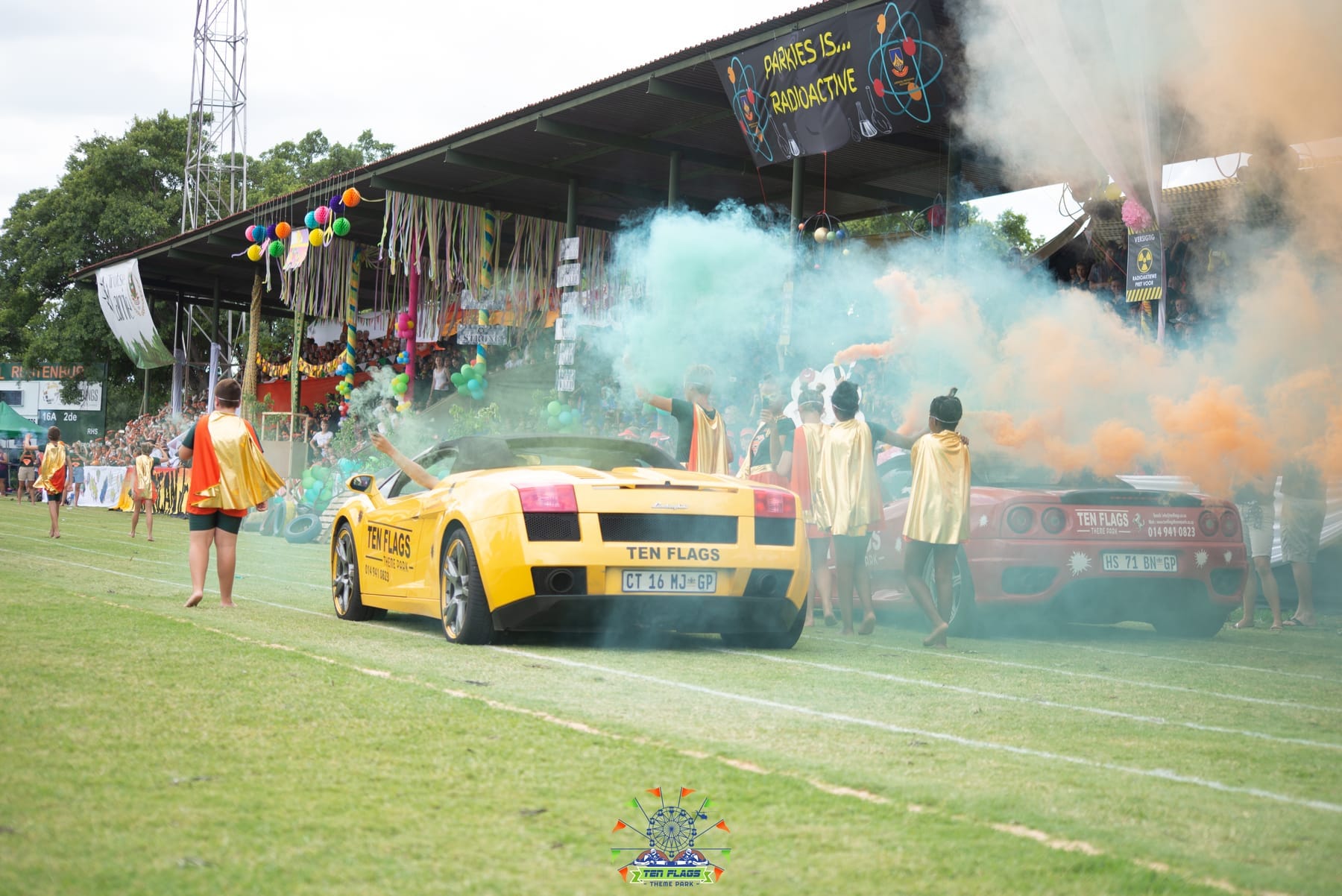 Yellow Lamborghini in a parade past a grandstand with coloured smoke