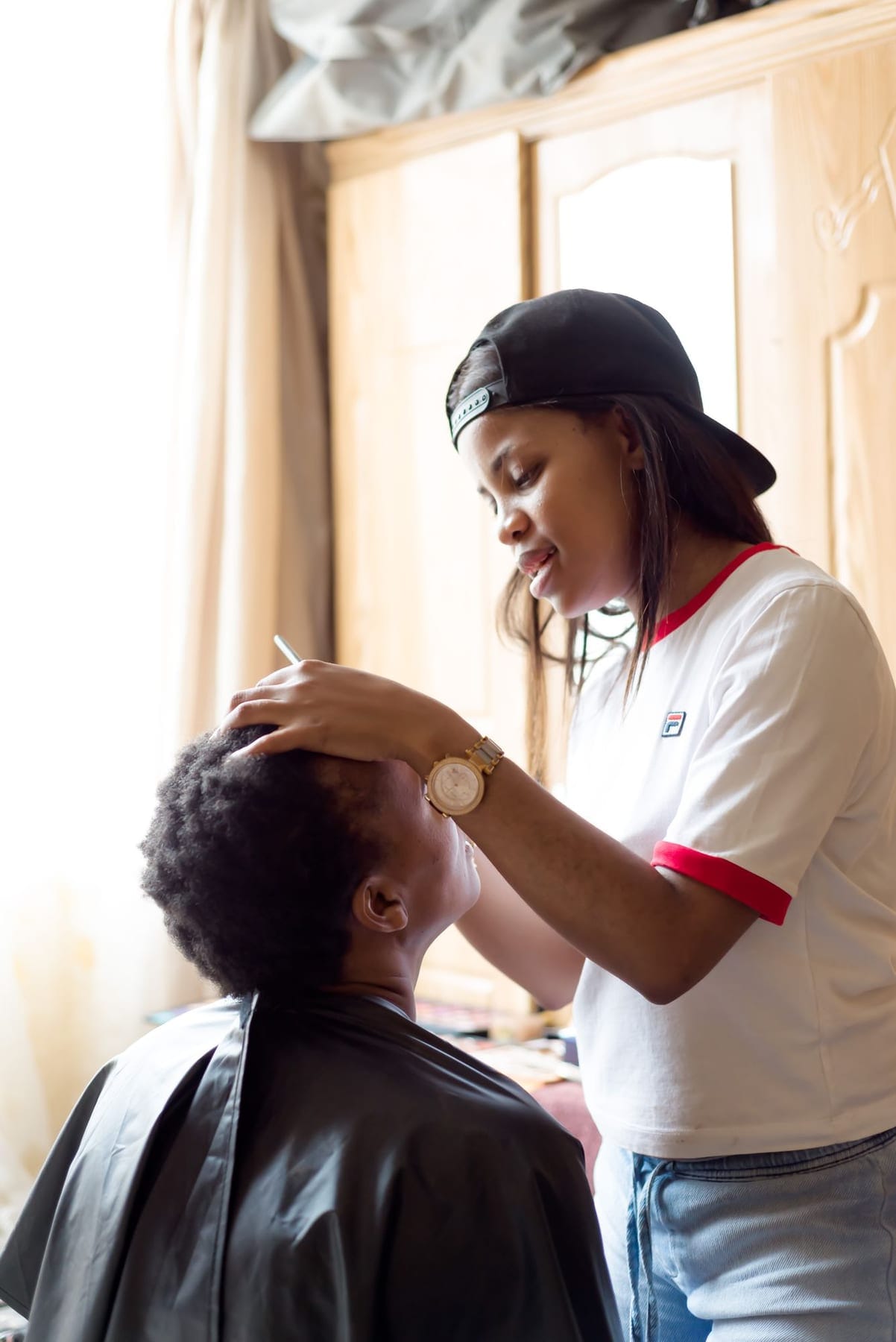 Makeup artist steadying a client's head as she lines her eyes, wardrobe behind