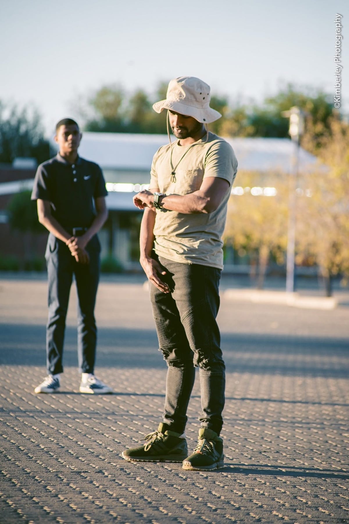 Bucket hat, arms folded, a friend behind