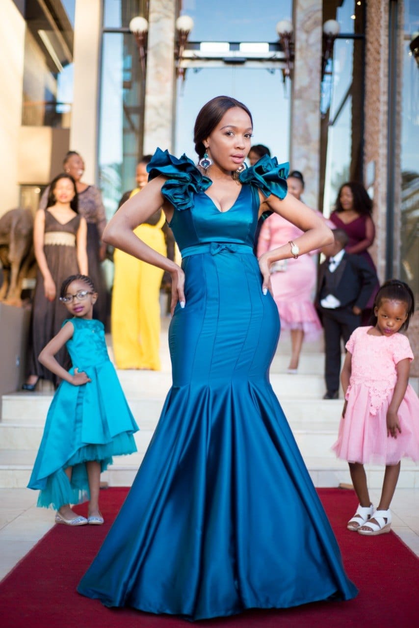 Teal ruffled gown on a red carpet, two flower girls posing