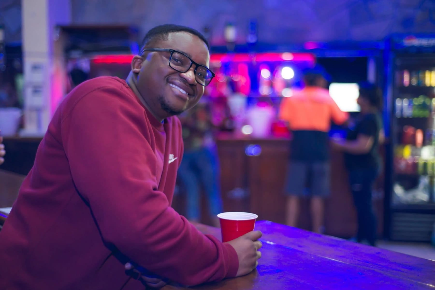 Sipping from a red cup at the bar under blue and pink light