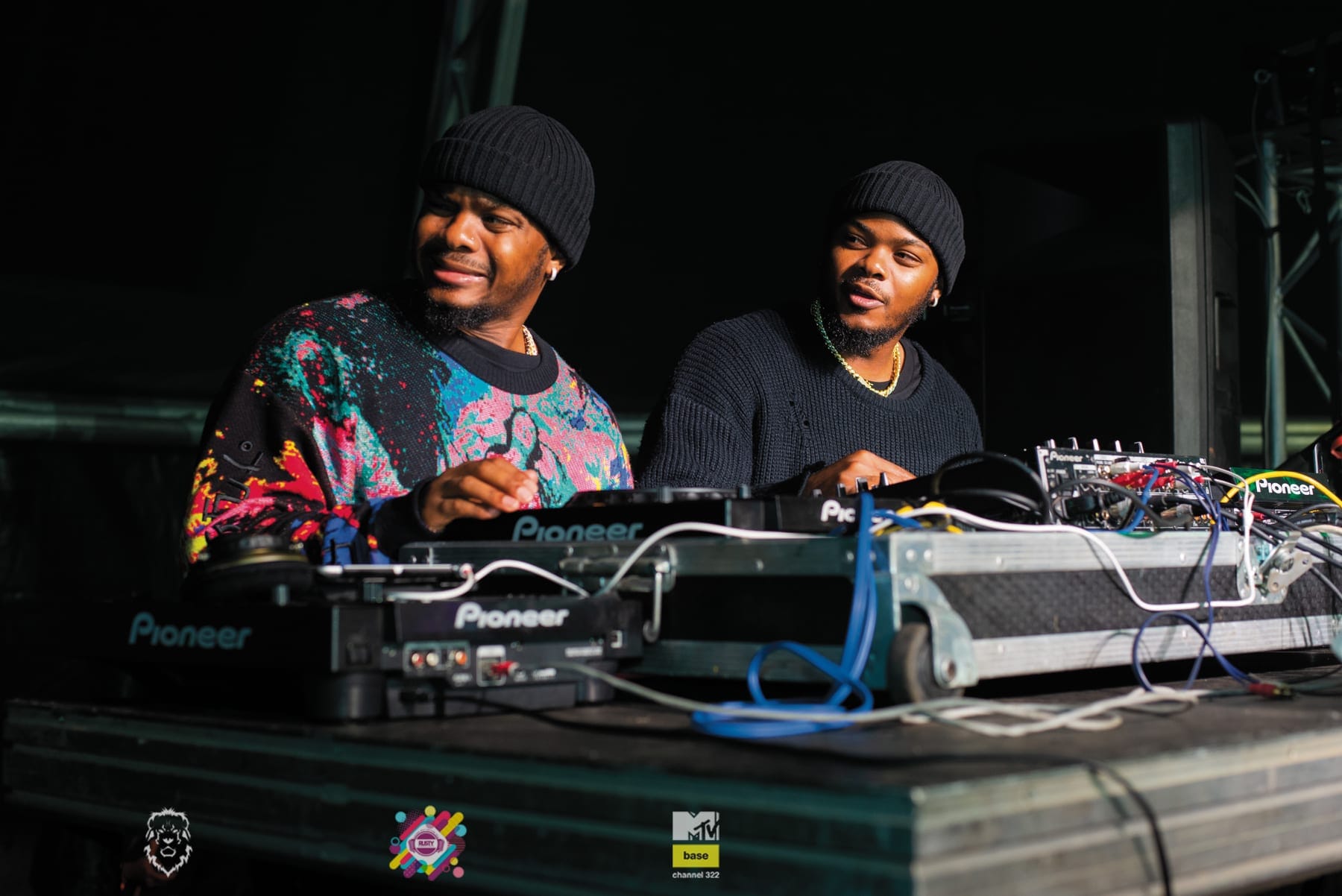 Two DJs in beanies grinning over the decks