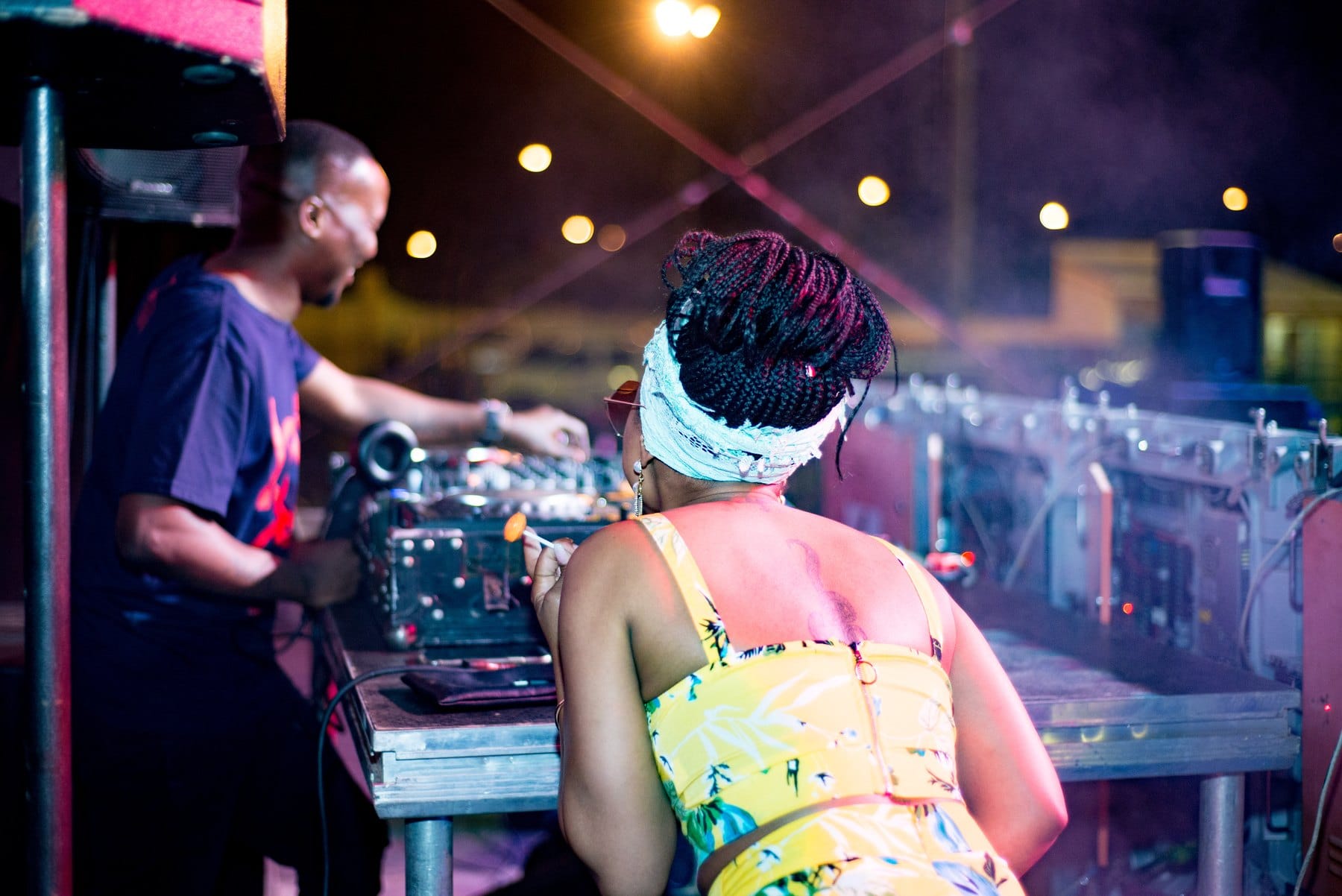 DJ at the decks with a guest leaning in, lollipop in hand