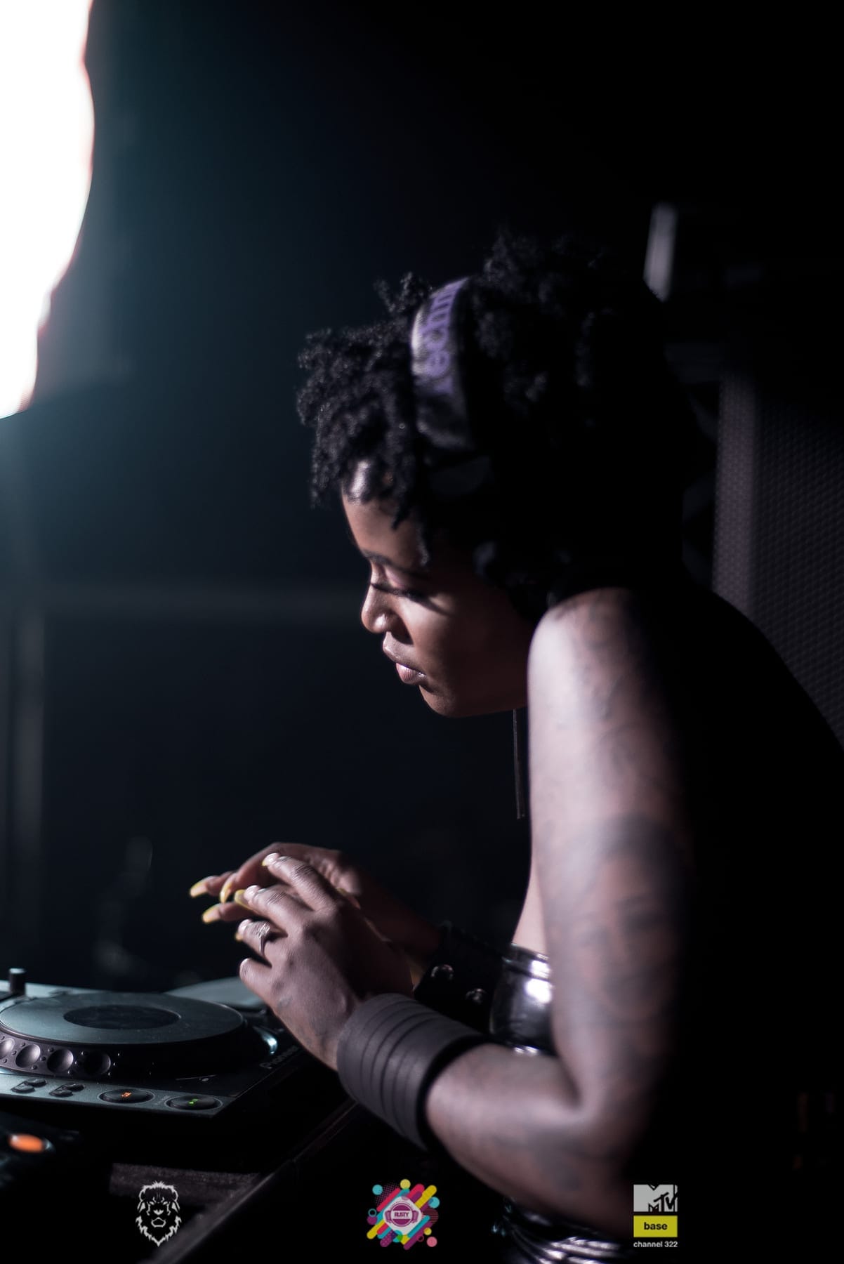 DJ in profile at the decks, light on her braids
