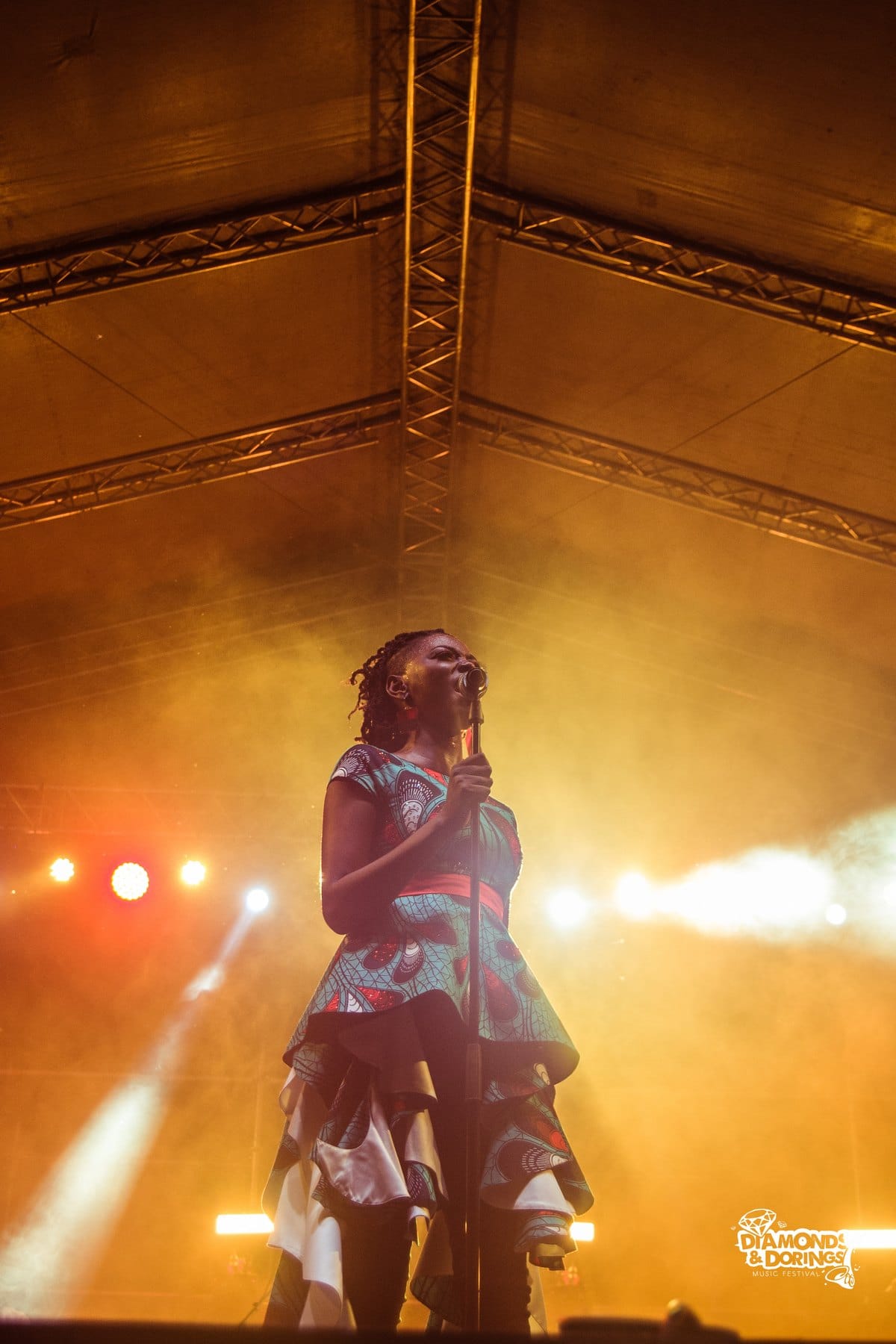 Singer in a patterned dress under an amber-lit stage roof