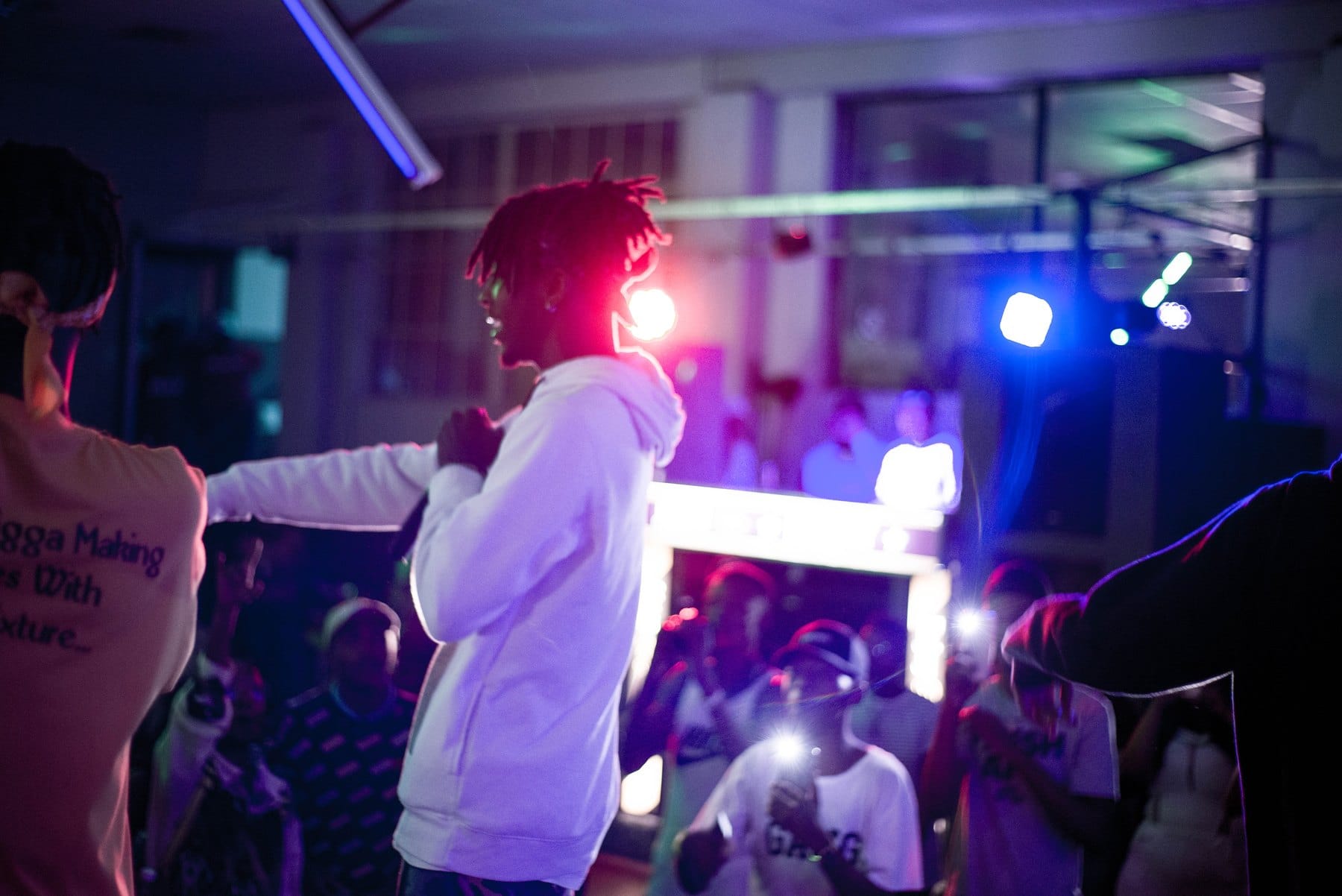 Rapper in a white hoodie lit pink at a club show