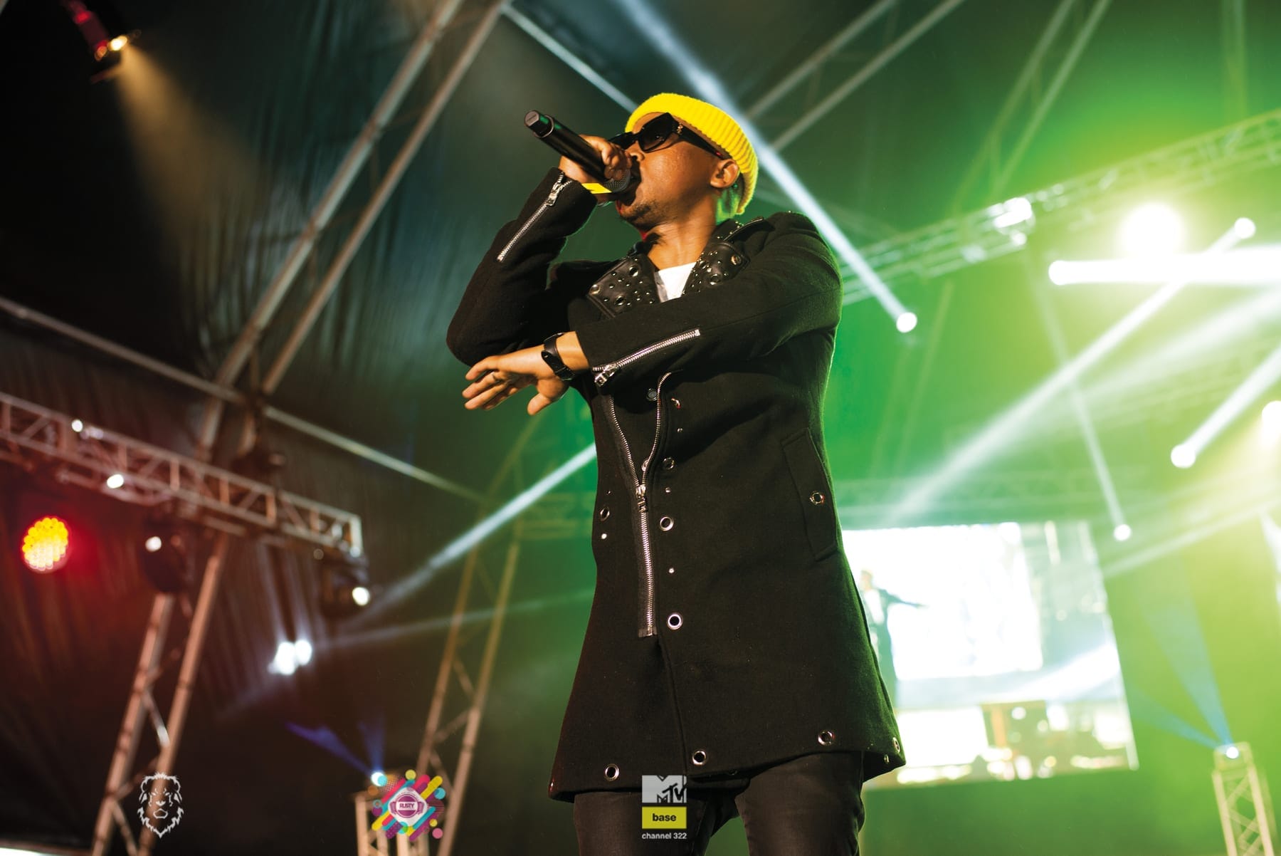 Rapper in a yellow cap mid-verse under green beams