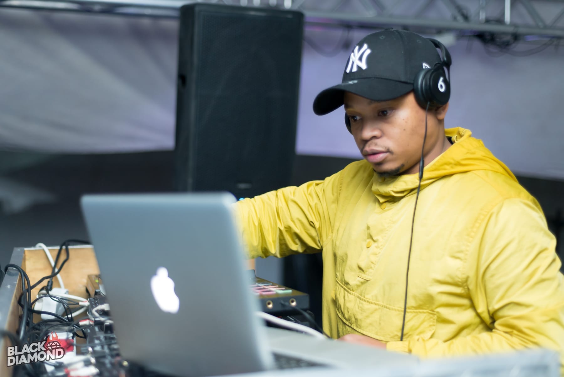 DJ in a yellow jacket and cap at a laptop and decks