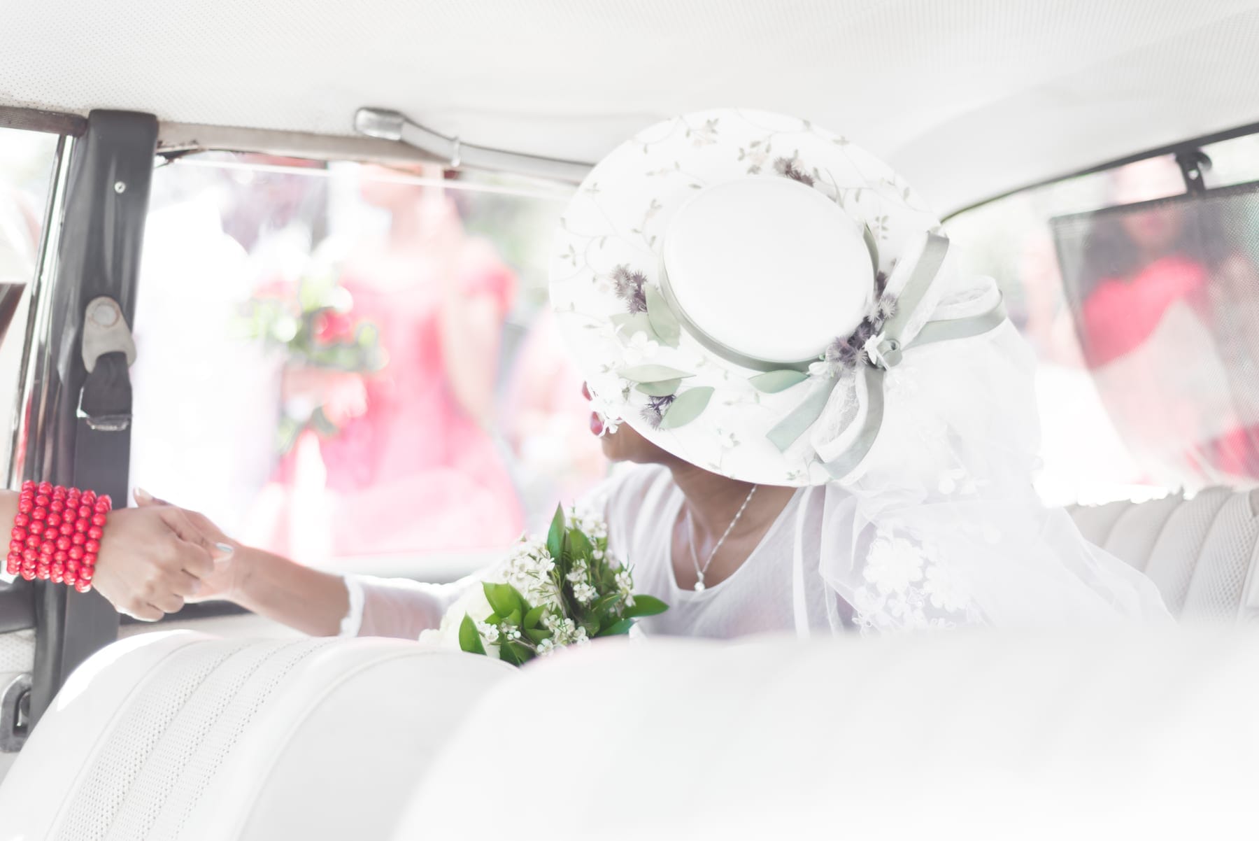 Bride in a white hat with her bouquet, arriving by car