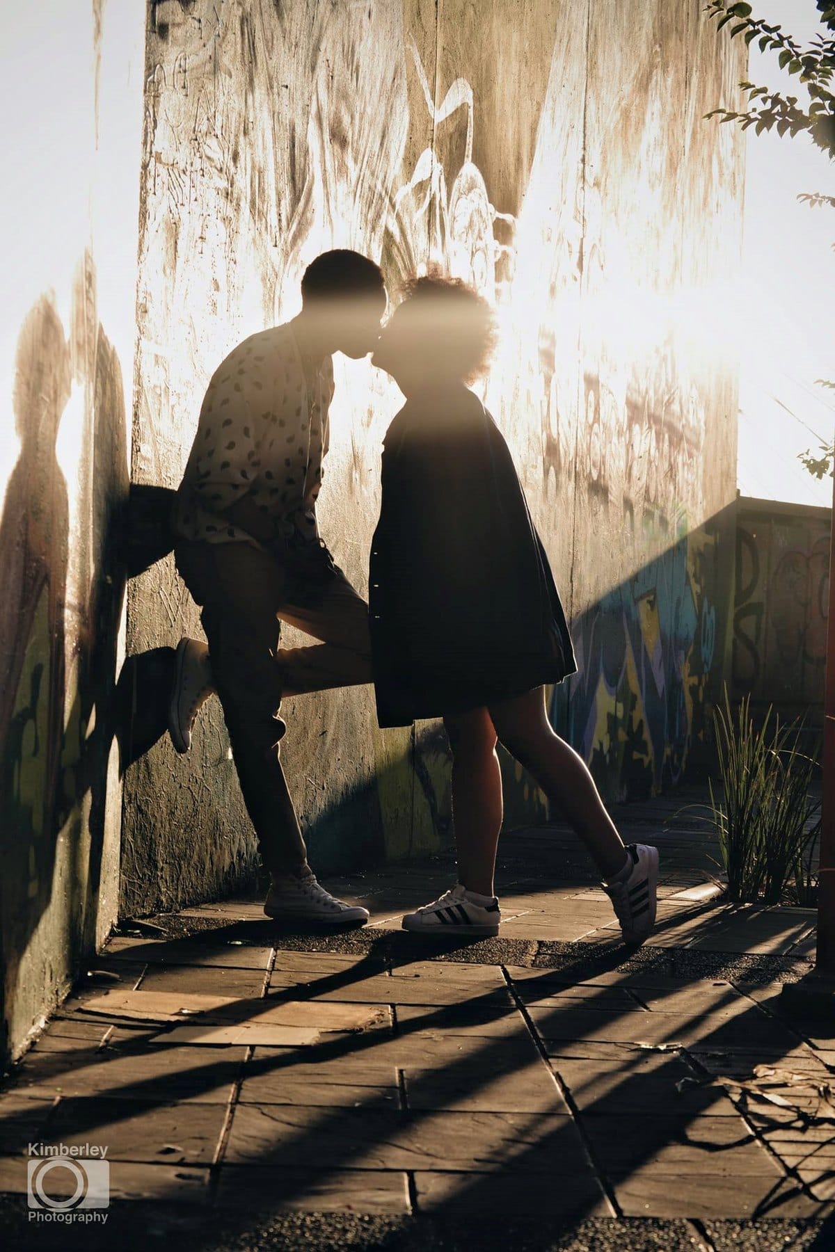 A kiss against a sunlit graffiti wall